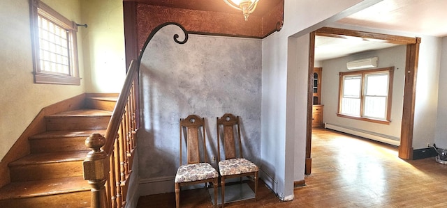 staircase with baseboard heating, an AC wall unit, baseboards, and wood finished floors