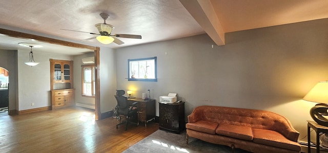 office space featuring wood finished floors, baseboards, a wall mounted AC, beam ceiling, and ceiling fan