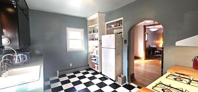 kitchen with arched walkways, tile patterned floors, a baseboard heating unit, and freestanding refrigerator