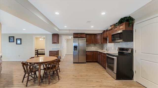 kitchen featuring baseboards, decorative backsplash, light wood-style flooring, appliances with stainless steel finishes, and a sink