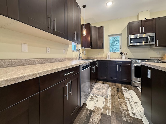 kitchen with dark wood-type flooring, decorative light fixtures, light countertops, stainless steel appliances, and a sink