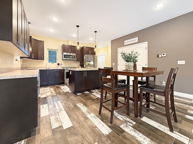 kitchen featuring wood finished floors, a sink, light countertops, dark brown cabinets, and appliances with stainless steel finishes