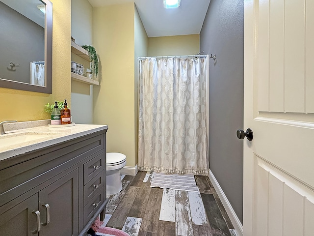 bathroom featuring baseboards, toilet, wood finished floors, and vanity