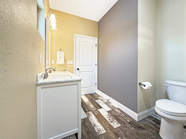 bathroom with toilet, vanity, baseboards, and wood finished floors