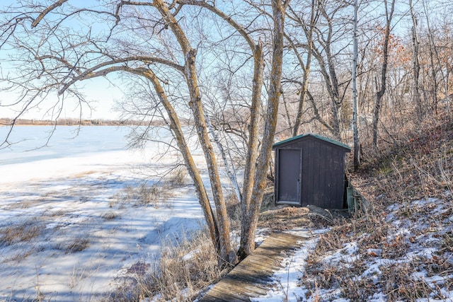 snow covered structure featuring a storage unit, a water view, and an outdoor structure