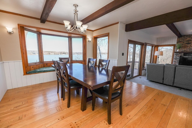 dining room featuring light wood finished floors, beam ceiling, wainscoting, a fireplace, and an inviting chandelier