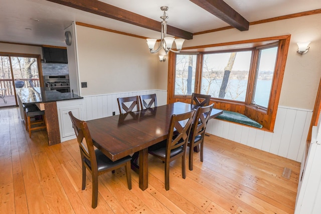 dining area featuring beam ceiling, a wainscoted wall, a healthy amount of sunlight, and light wood-style flooring