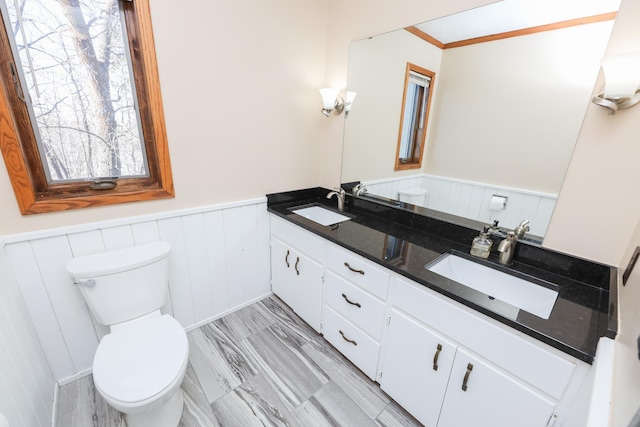 full bath featuring double vanity, a wainscoted wall, toilet, and a sink