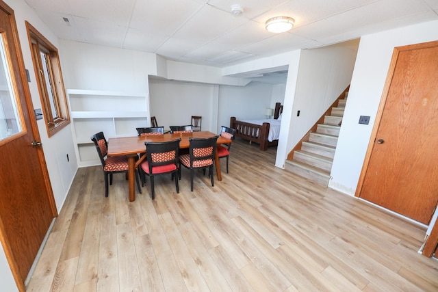 dining space featuring stairway, light wood-style floors, and a drop ceiling