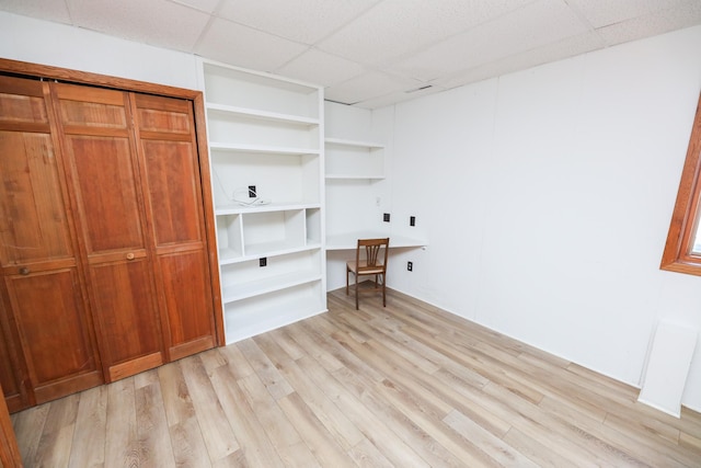 unfurnished office with built in desk, a paneled ceiling, and light wood-style floors