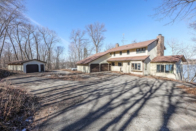 back of house featuring an outbuilding, a garage, driveway, and a chimney