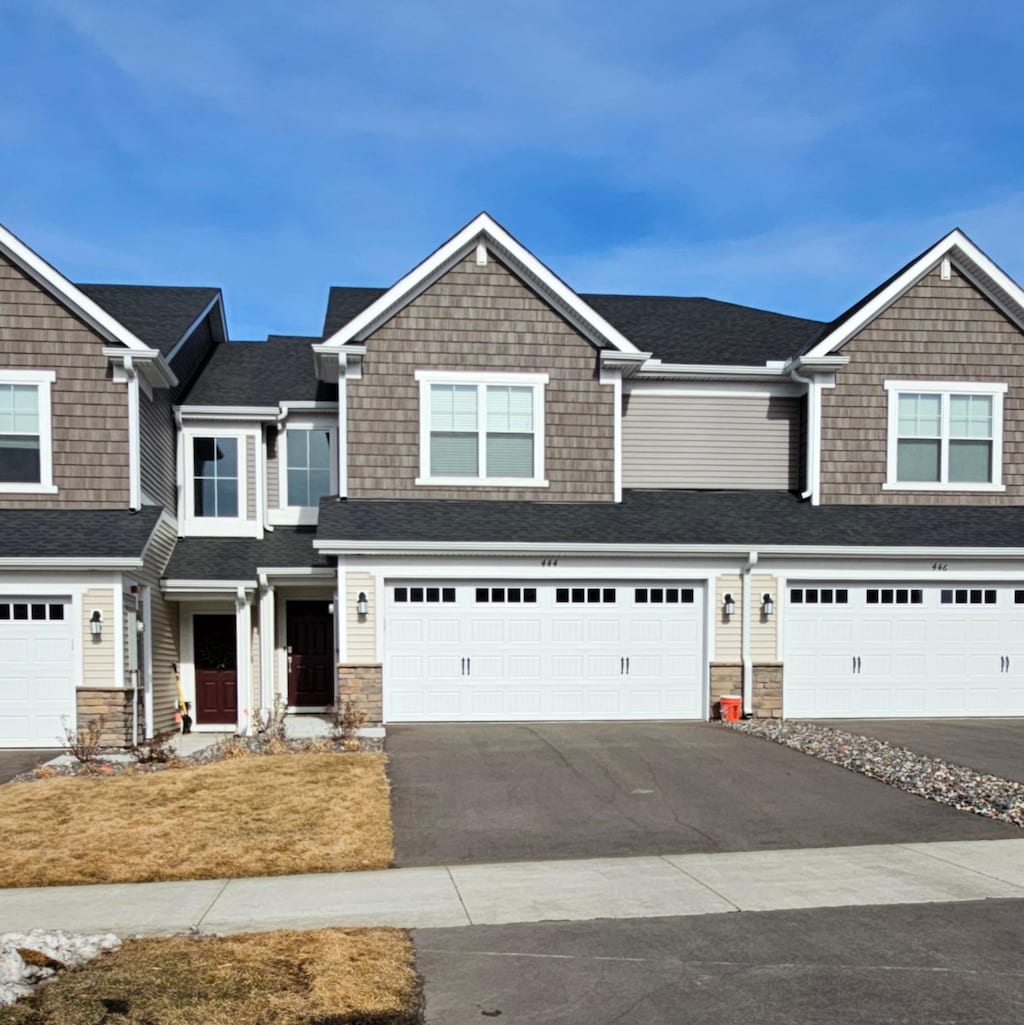 view of front facade featuring stone siding, driveway, an attached garage, and a shingled roof