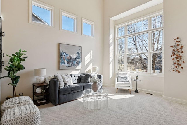 carpeted living room featuring a high ceiling, a healthy amount of sunlight, visible vents, and baseboards