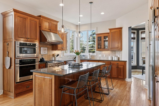 kitchen with brown cabinets, a breakfast bar, under cabinet range hood, a kitchen island, and range