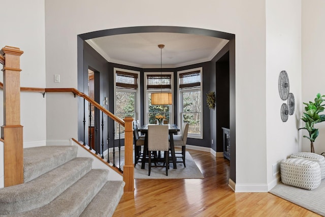 dining space with wood finished floors, baseboards, arched walkways, stairs, and crown molding