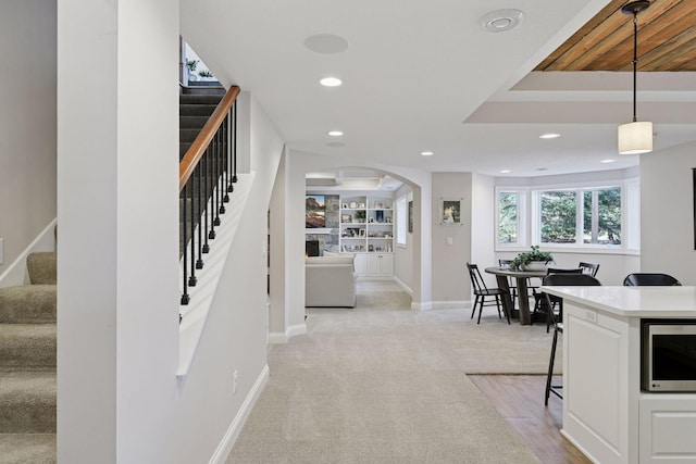 kitchen with recessed lighting, arched walkways, stainless steel microwave, a kitchen breakfast bar, and light colored carpet