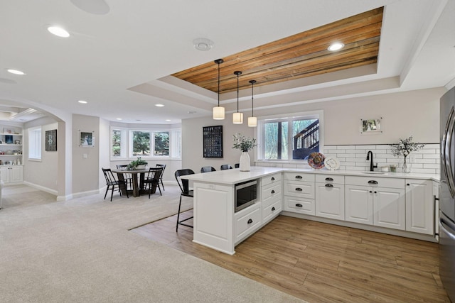 kitchen with a peninsula, a sink, a kitchen bar, stainless steel microwave, and a raised ceiling