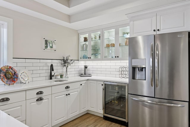 kitchen featuring beverage cooler, a sink, stainless steel fridge, glass insert cabinets, and tasteful backsplash