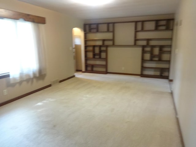 empty room with visible vents, light colored carpet, arched walkways, and baseboards