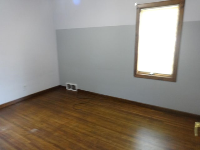 empty room featuring dark wood finished floors, visible vents, and baseboards