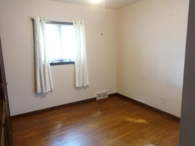 unfurnished room featuring dark wood finished floors, visible vents, and baseboards