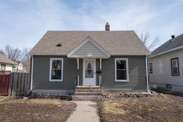 bungalow-style home featuring a shingled roof, fence, and a chimney