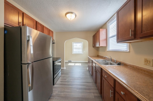 kitchen featuring baseboards, stainless steel appliances, wood finished floors, a textured ceiling, and a sink