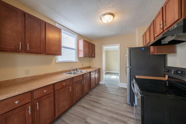 kitchen featuring light wood finished floors, under cabinet range hood, stainless steel electric stove, light countertops, and a sink