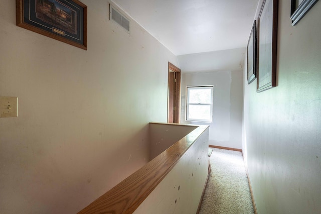 hall with an upstairs landing, light colored carpet, visible vents, and baseboards