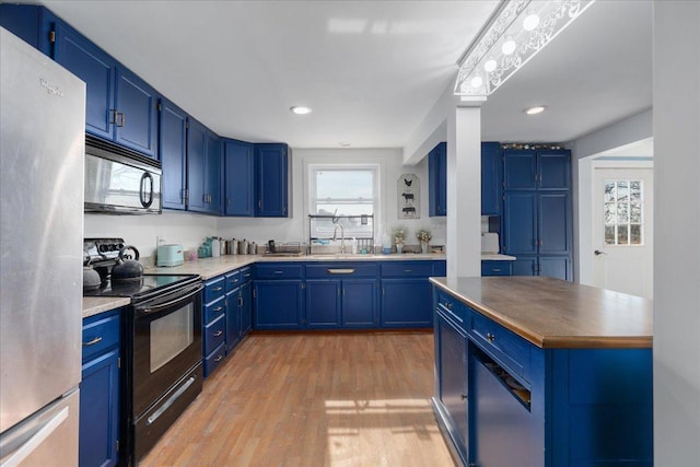 kitchen with blue cabinetry, a sink, black range with electric cooktop, freestanding refrigerator, and light wood finished floors