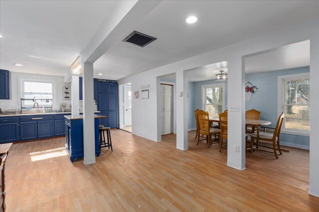 kitchen featuring blue cabinetry, visible vents, a breakfast bar, and light wood-style flooring