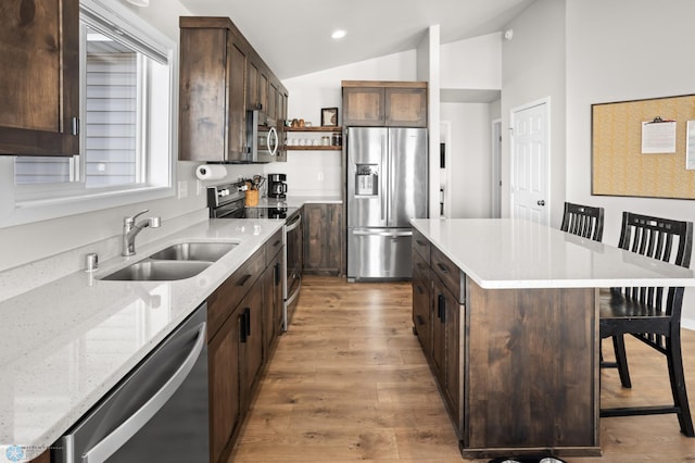 kitchen featuring a breakfast bar area, light wood-type flooring, vaulted ceiling, appliances with stainless steel finishes, and a sink