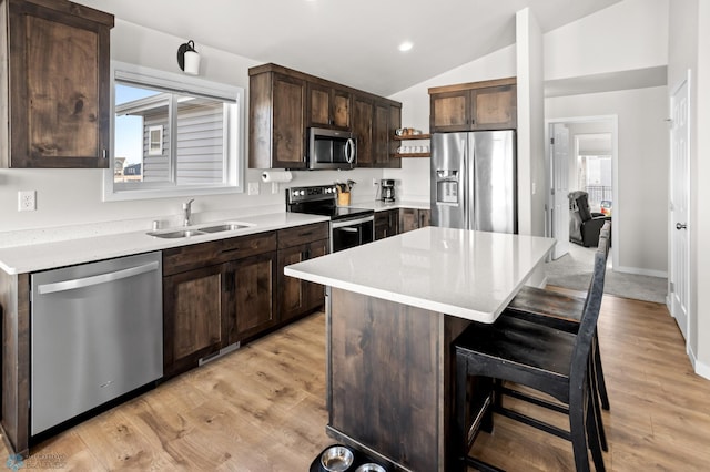 kitchen with a kitchen island, lofted ceiling, a sink, appliances with stainless steel finishes, and a kitchen bar