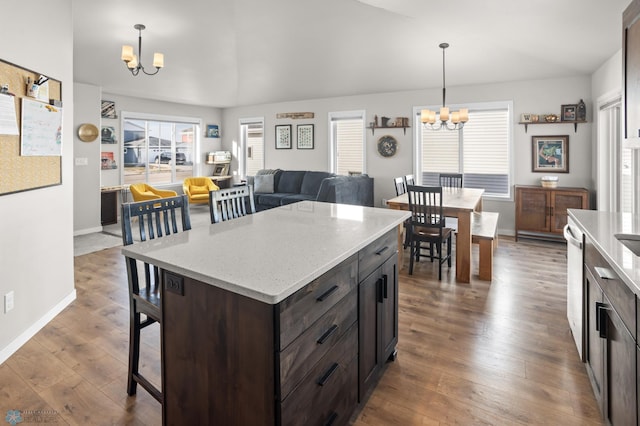 kitchen with a kitchen bar, wood-type flooring, dark brown cabinetry, an inviting chandelier, and hanging light fixtures