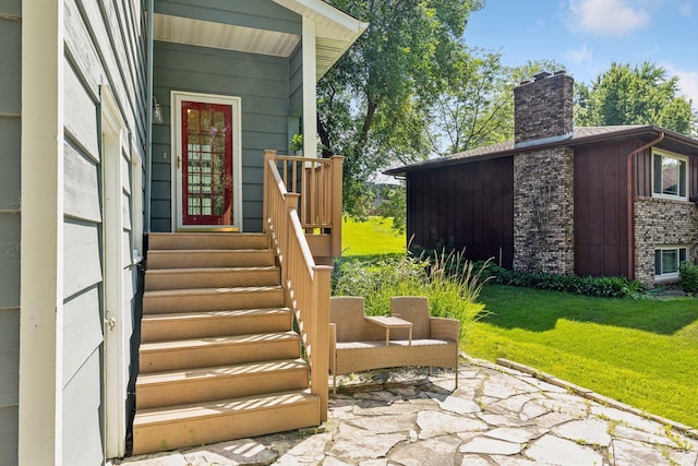 entrance to property featuring a lawn, a chimney, and a patio