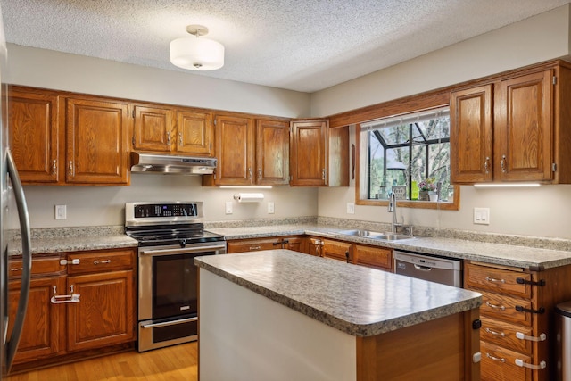 kitchen featuring appliances with stainless steel finishes, brown cabinets, under cabinet range hood, and a sink