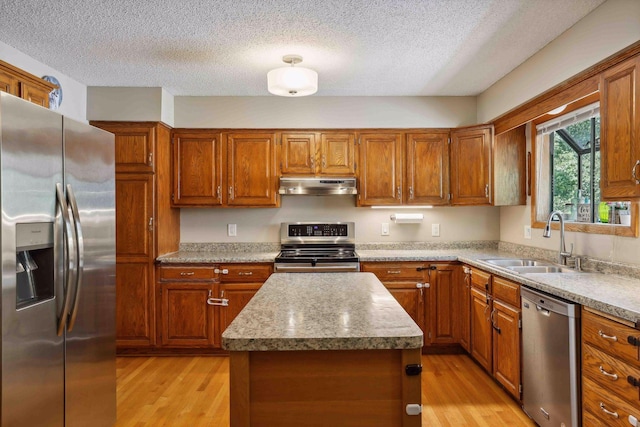 kitchen featuring under cabinet range hood, appliances with stainless steel finishes, light wood-type flooring, and a sink