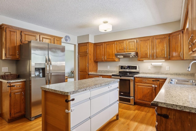 kitchen featuring light wood-style flooring, a sink, under cabinet range hood, a center island, and appliances with stainless steel finishes