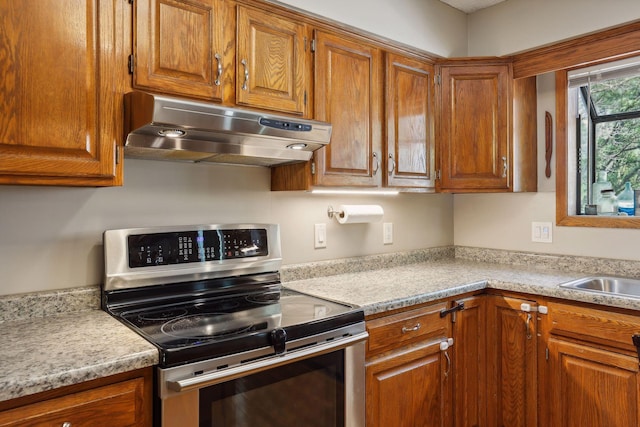 kitchen featuring under cabinet range hood, electric range, brown cabinets, and light countertops