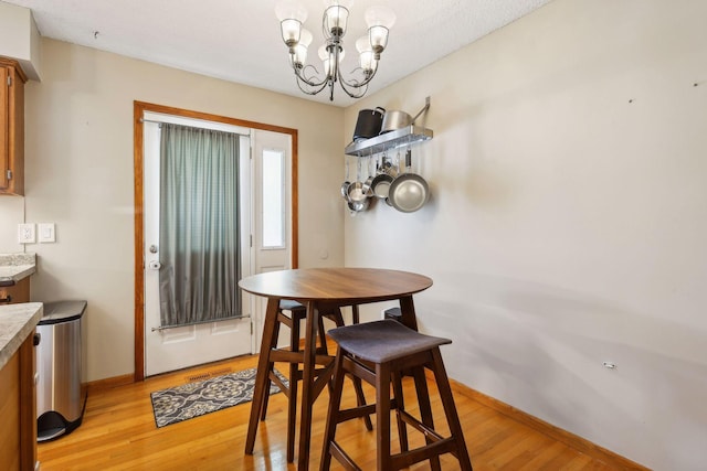 dining area with light wood-style flooring, a notable chandelier, and baseboards