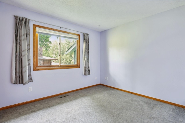 empty room with carpet flooring, visible vents, a textured ceiling, and baseboards