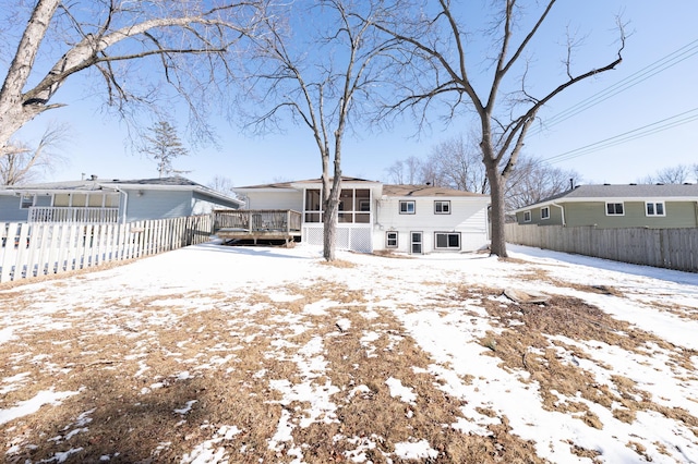 snow covered rear of property featuring a fenced backyard and a sunroom