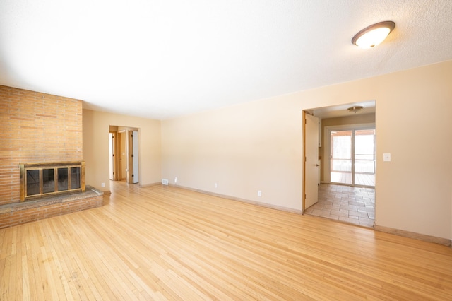 unfurnished living room featuring baseboards, a brick fireplace, and wood finished floors