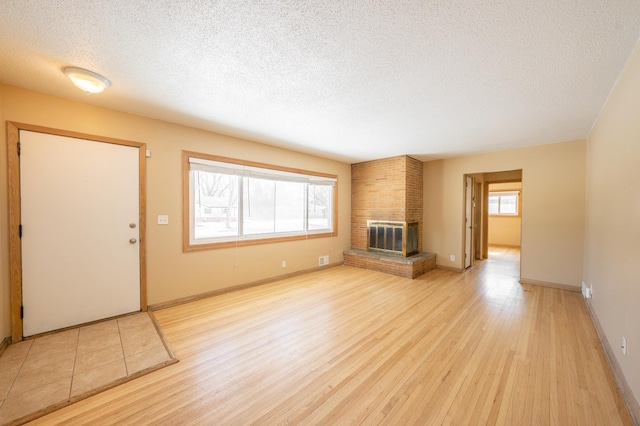 unfurnished living room with a brick fireplace, baseboards, light wood finished floors, and a textured ceiling