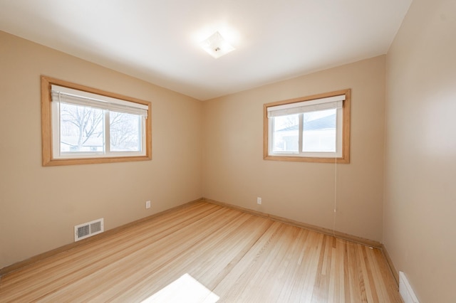 empty room with a wealth of natural light, visible vents, and wood finished floors