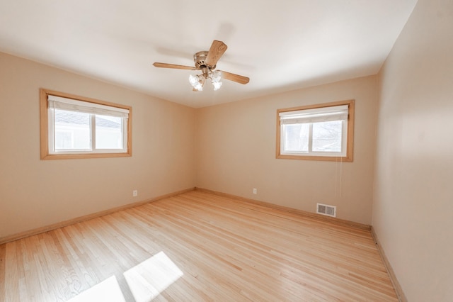 spare room featuring visible vents, plenty of natural light, baseboards, and wood finished floors