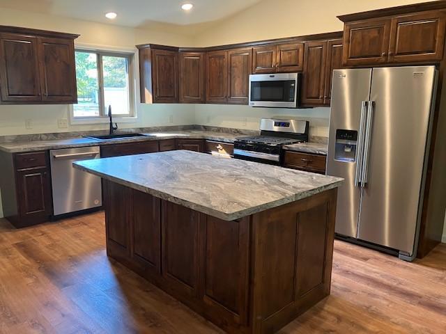 kitchen with light wood finished floors, dark brown cabinets, a center island, stainless steel appliances, and a sink