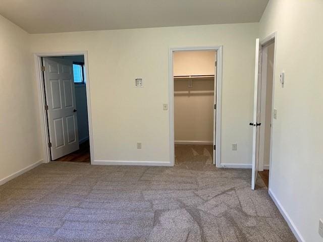 unfurnished bedroom featuring a spacious closet, a closet, baseboards, and carpet