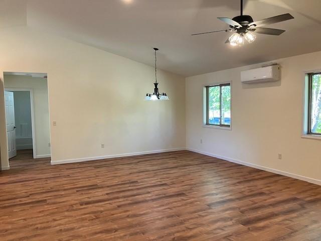 empty room featuring a wealth of natural light, wood finished floors, an AC wall unit, and vaulted ceiling