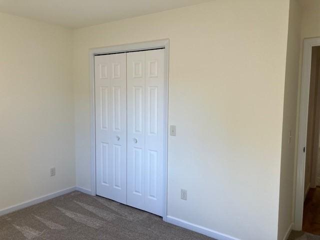 unfurnished bedroom featuring a closet, baseboards, and dark carpet